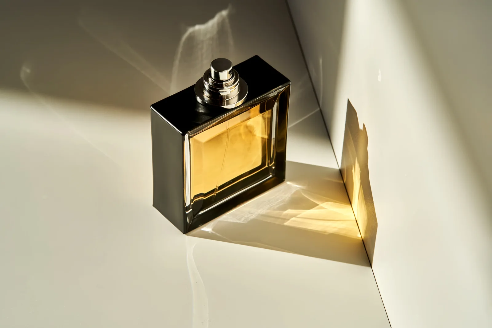 A rectangular amber perfume bottle and leaf casting soft sunlit shadows