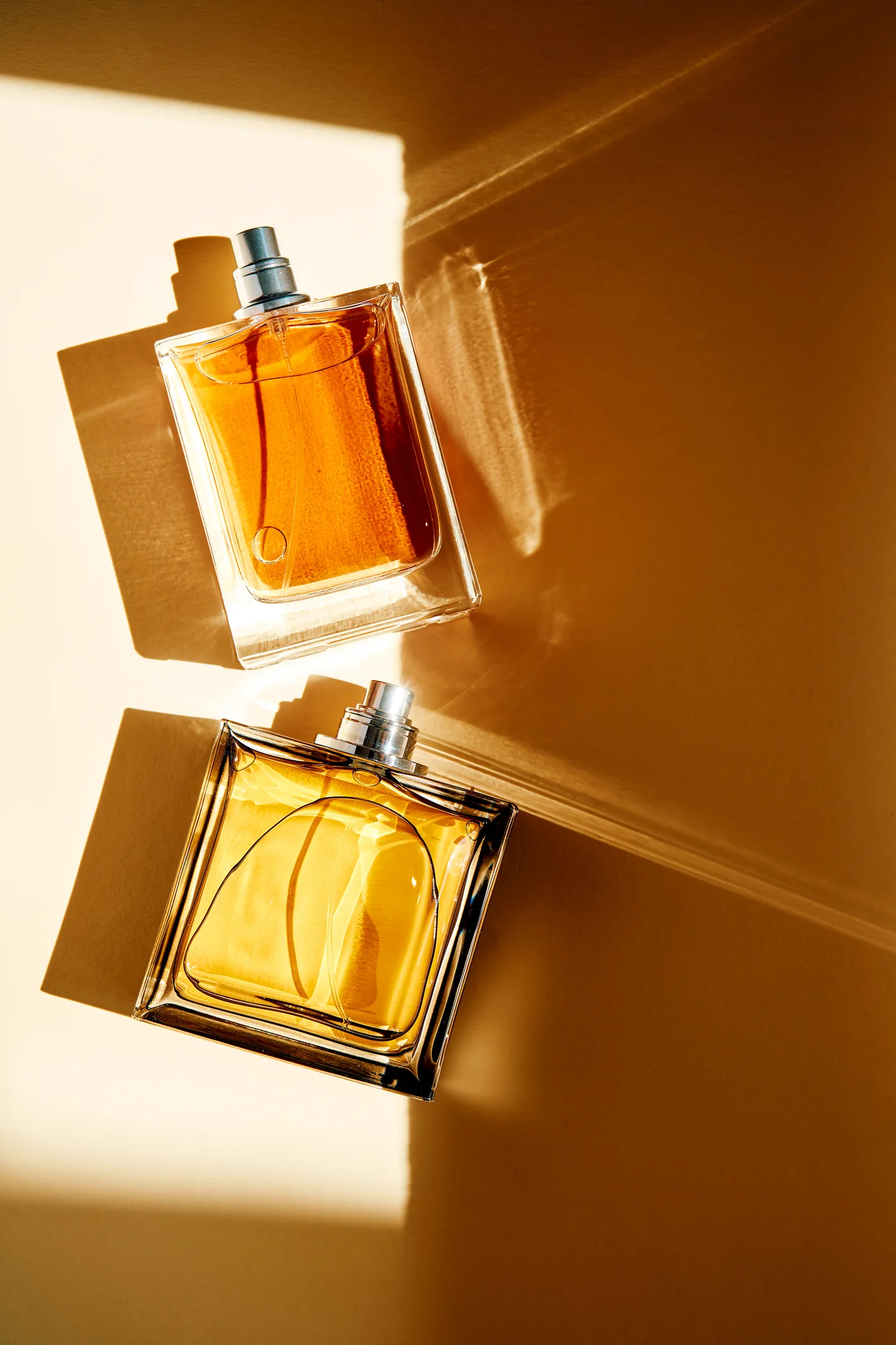 Two amber perfume bottles with long golden sunlight and shadows
