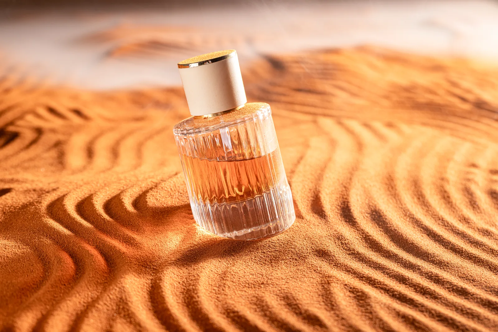 An amber perfume bottle resting on rippled golden sand